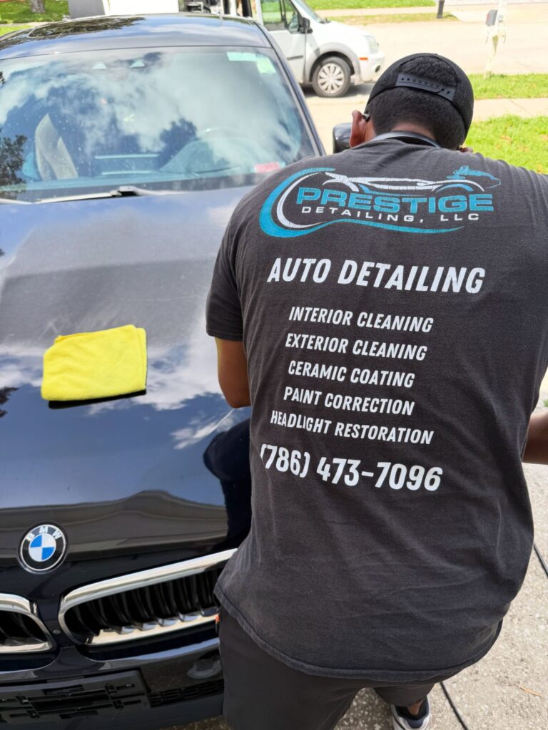 Prestige Detailing technician hand-detailing a black BMW in a customer driveway